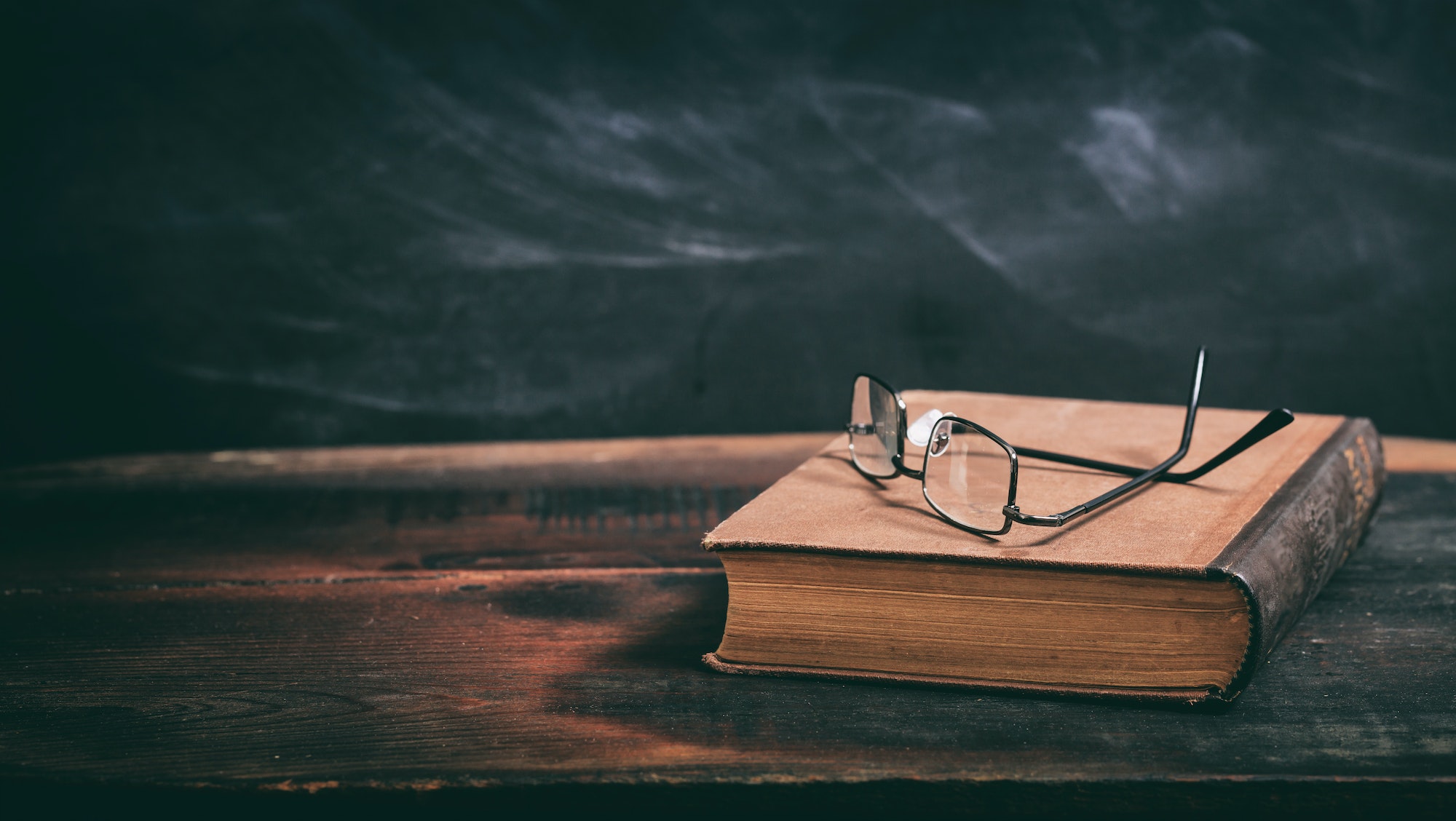 Old book and eye glasses on blackboard background